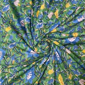 May include: Green fabric with a floral pattern. The design features blue, yellow, and white flowers and leaves on a green background. The fabric is gathered, creating folds and shadows that add depth to the design.