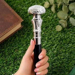 May include: A walking stick featuring a polished black shaft and a silver-toned metal handle. The handle is rounded with an intricate embossed floral pattern on the top and sides, transitioning into a smooth, tapered neck that connects to the shaft.