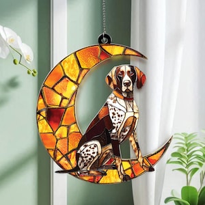 May include: Stained glass dog ornament featuring a German Shorthaired Pointer sitting on a crescent moon. The moon is made of orange and yellow glass pieces. The dog has brown, white, and black markings. A decorative hanging ornament.