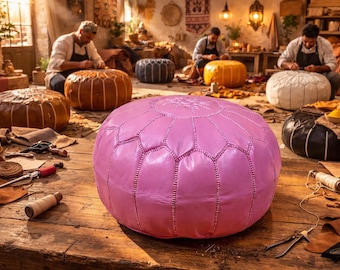 Può includere: Un grande pouf in pelle rosa con cuciture geometriche è in primo piano. Altri pouf in pelle marrone, nero, bianco e giallo sono sullo sfondo. La scena è un laboratorio con artigiani che lavorano la pelle.
