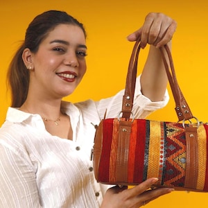 A unique boho crossbody bag featuring soft  leather and a vibrant kilim panel with red, yellow, and orange geometric patterns.