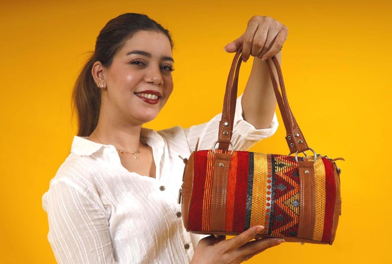 A unique boho crossbody bag featuring soft  leather and a vibrant kilim panel with red, yellow, and orange geometric patterns.