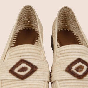 Puede incluir: Primer plano de dos mocasines beige tejidos. Cada zapato presenta un acento en forma de diamante marr&oacute;n en la parte superior y un dise&ntilde;o tejido. El interior es marr&oacute;n. Los zapatos son de color neutro, adecuados para varios atuendos.