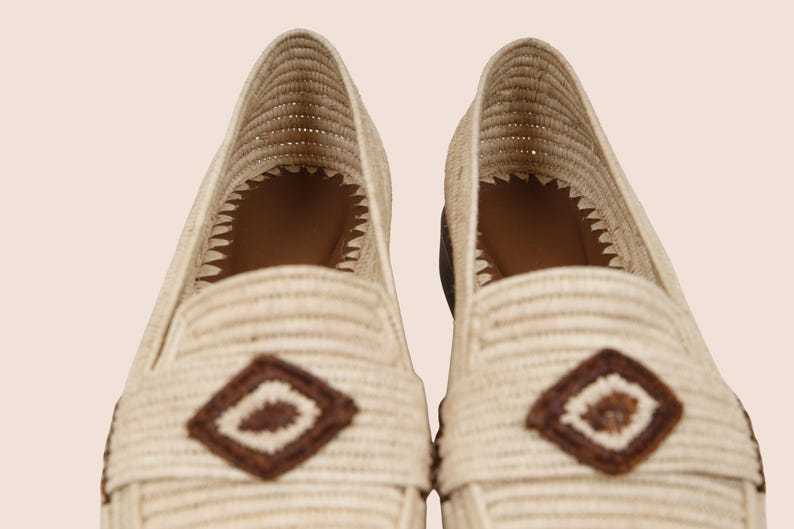 Puede incluir: Primer plano de dos mocasines beige tejidos. Cada zapato presenta un acento en forma de diamante marr&oacute;n en la parte superior y un dise&ntilde;o tejido. El interior es marr&oacute;n. Los zapatos son de color neutro, adecuados para varios atuendos.