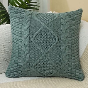 May include: A soft, green knitted throw pillow with a cable knit pattern. The pillow is square and has a diamond-shaped design in the center.
