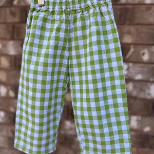 May include: Cropped trousers in a green and white gingham check pattern, hanging on a wooden hanger. The lightweight fabric features an elasticated waistband. The checkered design is a classic style, suitable for casual wear.