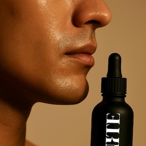 May include: Black bottle with a dropper, featuring the word "IGNITE" in white, and the word "ENCENDER" below it. The bottle is held near a person's face. The product appears to be a skincare serum.