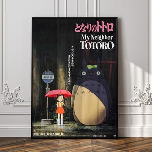 May include: A framed poster for the animated film "My Neighbor Totoro." The artwork depicts a young girl with a red umbrella standing in the rain next to a bus stop, with the large Totoro character. Japanese text is visible.