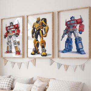 Könnte beinhalten: Drei gerahmte Drucke von Transformers-Charakteren: Optimus Prime in Rot und Blau, Bumblebee in Gelb und Schwarz und ein weiterer Optimus Prime. Die Drucke werden über einer Aufbewahrungsbank mit weißen Behältern und dekorativen Kissen angezeigt.