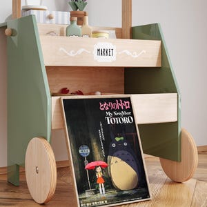 May include: A wooden toy market cart with green accents, featuring a poster for "My Neighbor Totoro." The cart has shelves with toy accessories and wooden wheels. The poster shows Totoro and a girl with an umbrella.