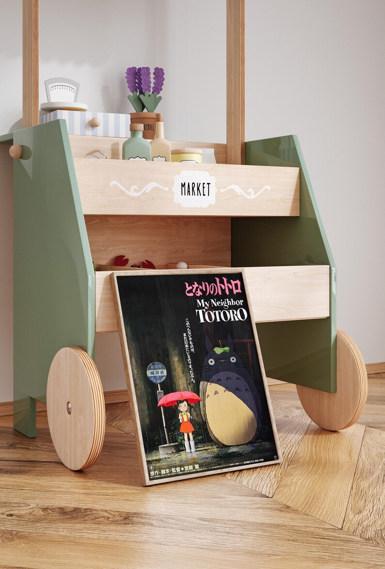 May include: A wooden toy market cart with green accents, featuring a poster for "My Neighbor Totoro." The cart has shelves with toy accessories and wooden wheels. The poster shows Totoro and a girl with an umbrella.
