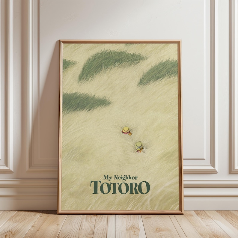 May include: A framed print featuring the text "My Neighbor Totoro" in green. The artwork depicts two figures in straw hats in a field of tall grass. The background is a light beige color, and the frame is a light brown.