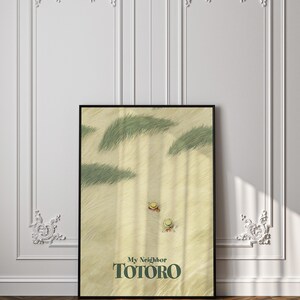 May include: A framed poster featuring a scene from "My Neighbor Totoro." The artwork depicts a sandy landscape with green grass and two figures wearing hats. The title "My Neighbor Totoro" is displayed in green text.