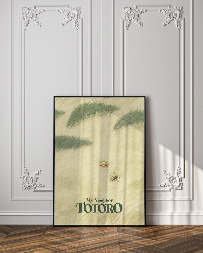 May include: A framed poster featuring a scene from "My Neighbor Totoro." The artwork depicts a sandy landscape with green grass and two figures wearing hats. The title "My Neighbor Totoro" is displayed in green text.