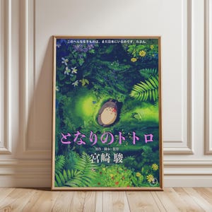 Peut inclure: Affiche encadr&eacute;e du film d'animation "Mon Voisin Totoro". L'&oelig;uvre repr&eacute;sente Totoro dans un cadre forestier avec du texte japonais. L'affiche a un cadre en bois et est affich&eacute;e contre un mur blanc.