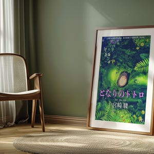 Peut inclure: A framed poster of the animated film "Mon Voisin Totoro." The illustration shows Totoro in a green forest, with Japanese text. The poster is displayed in a room with a wooden chair and a round rug, creating a warm atmosphere.