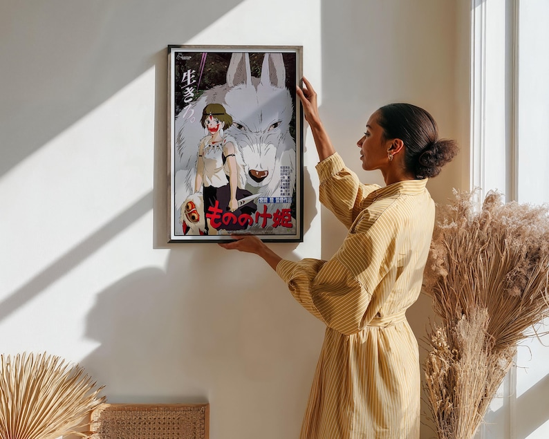 May include: Framed poster featuring anime artwork. The image showcases a girl with a wolf, with Japanese text. The poster has a black frame and is being held up against a white wall. The artwork is colorful, with a focus on the characters and their expressions.