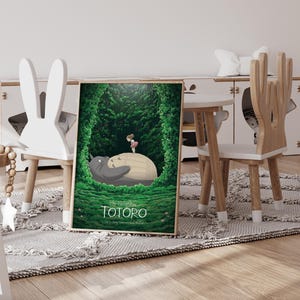 May include: A framed poster featuring a scene from "My Neighbor Totoro." The artwork depicts Totoro, a large gray forest spirit, with a young girl in a forest setting. The poster is displayed in a child's room with wooden furniture.