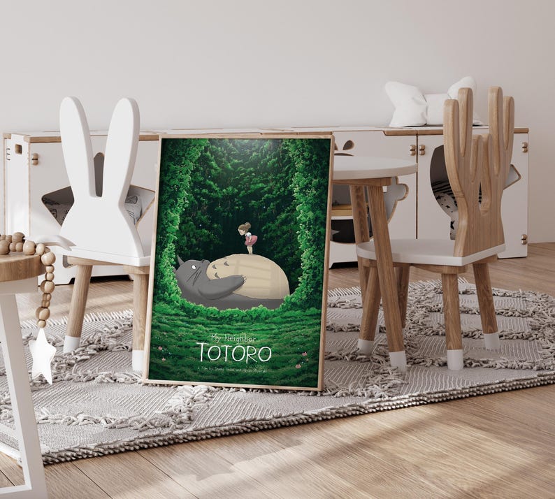 May include: A framed poster featuring a scene from "My Neighbor Totoro." The artwork depicts Totoro, a large gray forest spirit, with a young girl in a forest setting. The poster is displayed in a child's room with wooden furniture.