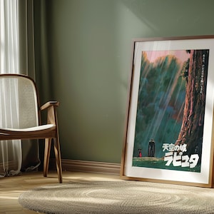 May include: A framed poster featuring Japanese text and a landscape scene with figures. The poster is leaning against a green wall in a room with a wooden chair, a round rug, and a potted plant. The poster has a wooden frame.