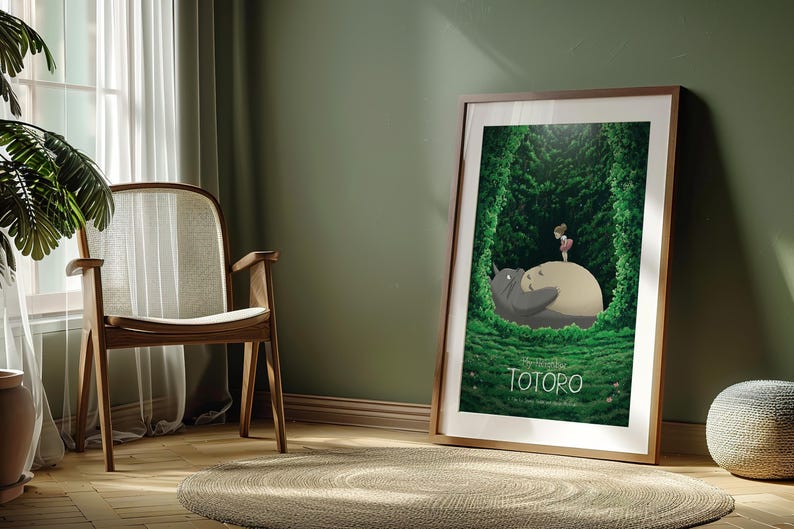 May include: Framed poster featuring a scene from "My Neighbor Totoro." The artwork depicts Totoro and a small girl in a lush green forest setting. The poster is in a wooden frame and leans against a green wall.