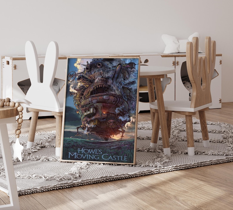Op de afbeelding: Ingelijste poster van Howl's Moving Castle, met een gedetailleerde illustratie van het kasteel met een vurige gloed aan de basis. De poster wordt weergegeven op een vloerkleed in een kinderkamer, naast houten meubels en een kleine tafel.