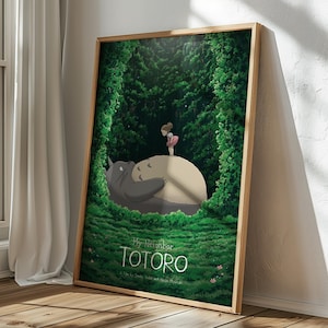 May include: A framed poster featuring a scene from "My Neighbor Totoro." The artwork depicts Totoro, a large gray forest spirit, lying down with a young girl standing on his belly. Lush green foliage surrounds them, with the title of the film at the bottom.