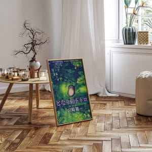 Peut inclure: Une affiche encadr&eacute;e avec du texte japonais, pr&eacute;sentant une illustration color&eacute;e de for&ecirc;t. L'&oelig;uvre d'art repr&eacute;sente un personnage central dans un environnement verdoyant. L'affiche est pos&eacute;e sur un sol en bois, pr&egrave;s d'une fen&ecirc;tre.