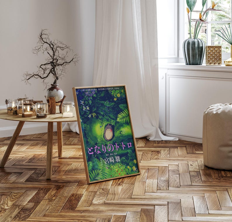 Peut inclure: Une affiche encadr&eacute;e avec du texte japonais, pr&eacute;sentant une illustration color&eacute;e de for&ecirc;t. L'&oelig;uvre d'art repr&eacute;sente un personnage central dans un environnement verdoyant. L'affiche est pos&eacute;e sur un sol en bois, pr&egrave;s d'une fen&ecirc;tre.