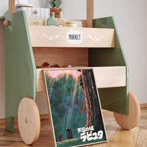 May include: A wooden toy market cart painted in green and natural wood tones. The cart features a framed poster with Japanese text and a colorful illustration. The cart has wooden wheels and shelves with toy accessories.