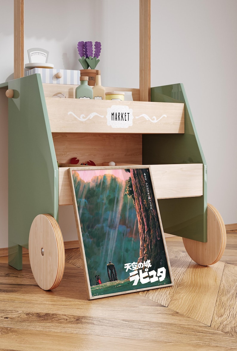 May include: A wooden toy market cart painted in green and natural wood tones. The cart features a framed poster with Japanese text and a colorful illustration. The cart has wooden wheels and shelves with toy accessories.