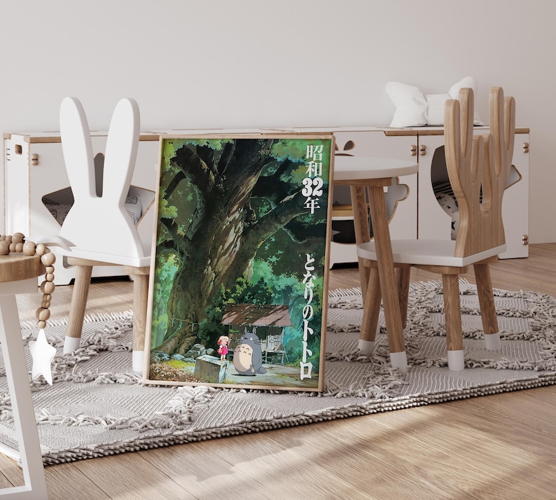Pu&ograve; includere: Un poster incorniciato con una scena del film d'animazione "Il mio vicino Totoro". L'opera raffigura un grande albero, una ragazza e Totoro. Il poster &egrave; esposto su un tappeto vicino a un tavolo e sedie bianche.