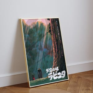 May include: Framed poster featuring artwork from the animated film "Castle in the Sky." The image depicts a towering robot, a small figure, and Japanese text against a backdrop of a forest and sky. The poster is in a gold frame.