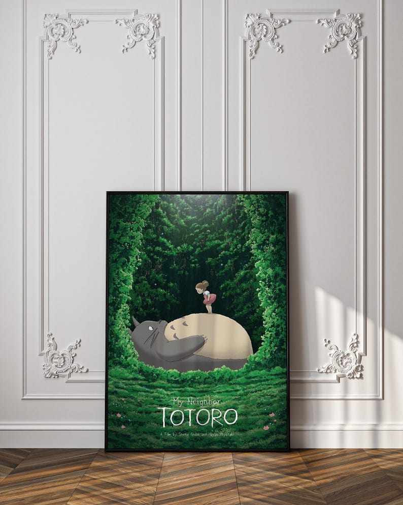 May include: A framed poster featuring the animated film "My Neighbor Totoro." The artwork depicts Totoro, a large gray forest spirit, with a young girl standing on his belly. Lush green foliage surrounds them, with the film's title at the bottom.