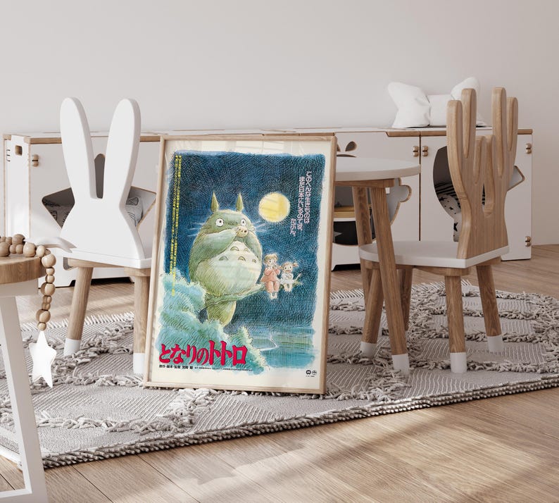 Puede incluir: P&oacute;ster enmarcado con una criatura verde y peluda sosteniendo una hoja, con una luna amarilla de fondo. Se ve texto japon&eacute;s. El p&oacute;ster est&aacute; en una habitaci&oacute;n infantil, junto a una silla blanca con forma de conejo.