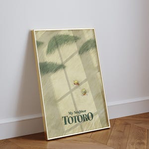 May include: A framed art print featuring a scene from "My Neighbor Totoro." The artwork depicts a field with two small figures wearing hats, with the title "My Neighbor Totoro" in green text at the bottom. The frame is gold.