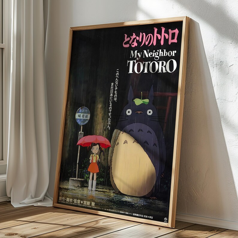 May include: A framed poster featuring the animated film "My Neighbor Totoro." The artwork depicts a young girl with a red umbrella, standing near a bus stop with Totoro, a large, friendly forest spirit, in a rainy scene. The title is in English and Japanese.