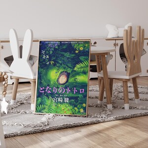 Peut inclure: A framed poster of the animated film "My Neighbor Totoro" with a forest scene and the character Totoro. The poster is displayed in a child's room with unique chairs and a small table. The room has a rug and a white cabinet.