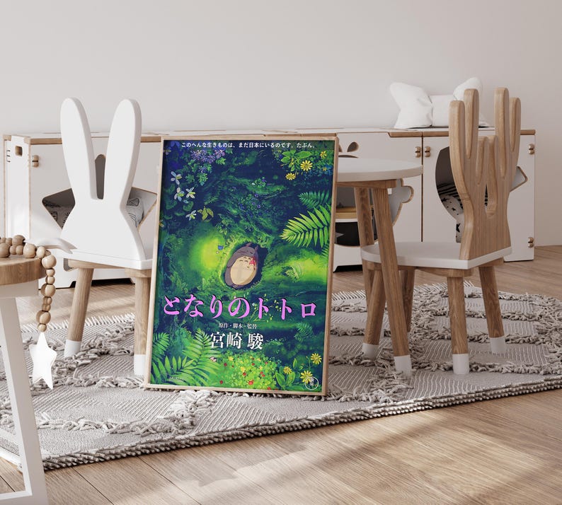 Peut inclure: A framed poster of the animated film "My Neighbor Totoro" with a forest scene and the character Totoro. The poster is displayed in a child's room with unique chairs and a small table. The room has a rug and a white cabinet.