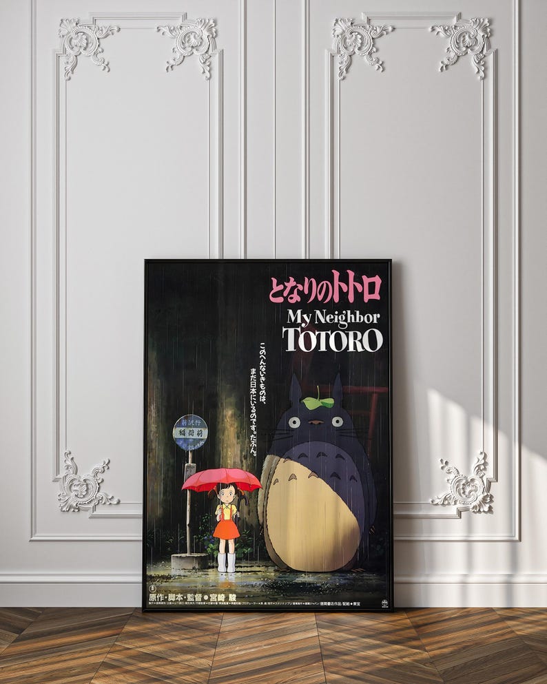 May include: A framed poster for the animated film "My Neighbor Totoro." The artwork depicts a young girl with a red umbrella standing in the rain next to a bus stop, with the large Totoro character. Japanese text is visible.