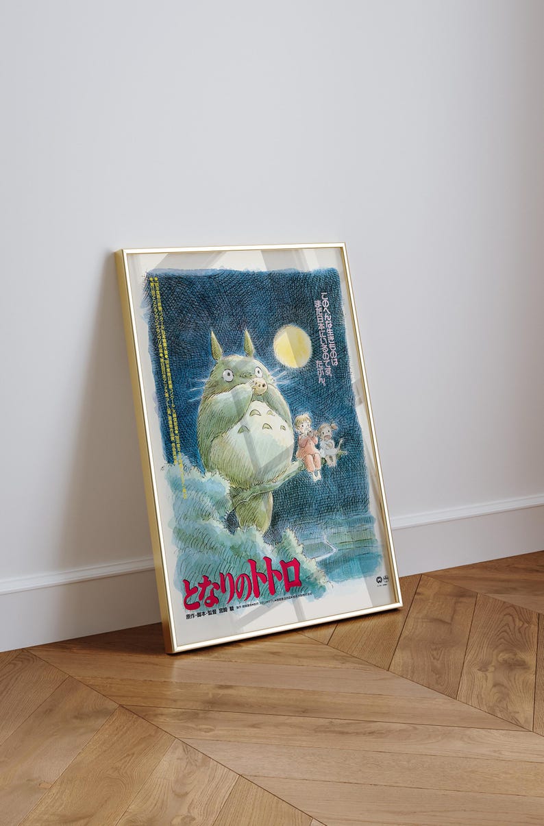 Puede incluir: P&oacute;ster enmarcado de la pel&iacute;cula de animaci&oacute;n "Mi vecino Totoro". La obra de arte representa a Totoro, un gran esp&iacute;ritu del bosque, con dos ni&ntilde;os y un cielo nocturno iluminado por la luna. El p&oacute;ster est&aacute; en un marco dorado y se apoya en una pared blanca.