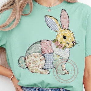 Könnte beinhalten: Hellgrünes T-Shirt mit einem Patchwork-Hasen-Design. Der Hase besteht aus verschiedenen Stoffmustern, darunter Blumenmuster, Vichy-Karo und Spitze. Er hat einen gelben Körper mit Blumenmuster, rosa und blaue Ohren und ist mit kleinen rosa Rosen verziert.