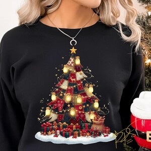 May include: Black sweatshirt with a festive Christmas tree design. The tree is adorned with fairy lights, a star, and gifts. The design has a patchwork style with red, blue, and white colors, creating a cozy holiday feel.
