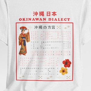 May include: White t-shirt featuring a graphic with Japanese text and a woman in traditional Okinawan attire. The design includes red and yellow flowers, and the words "OKINAWAN DIALECT" are displayed prominently.