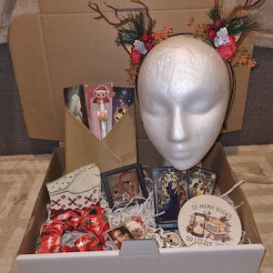 May include: A gift box filled with various items, including a reindeer antler headband, socks, scrunchies, tarot cards, stickers, and a decorative coaster with the text "So Many Books So Little Time."