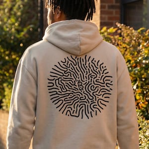 Puede incluir: Sudadera con capucha beige con un diseño circular negro en la espalda. El diseño es un patrón abstracto de líneas y curvas. La sudadera con capucha tiene una capucha y un ajuste relajado.