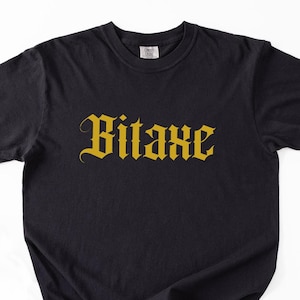 May include: Black t-shirt featuring the word "Bitaxe" in gold, gothic font. The short-sleeved shirt is made of a soft material. The text is centered on the chest.
