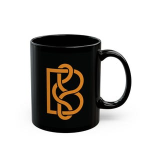 Puede incluir: Taza de cerámica negra con un diseño dorado entrelazado de "B" y "S". La taza tiene un cuerpo redondeado y un asa grande y curvada. El diseño está centrado en la superficie de la taza.