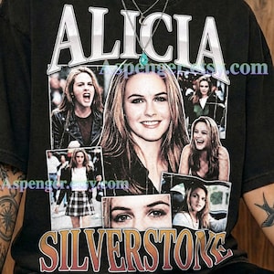 May include: A graphite-colored short-sleeve t-shirt featuring a collage of photographs of Alicia Silverstone. The text ALICIA appears in white at the top, and SILVERSTONE is printed in a gradient orange-to-white font at the bottom.