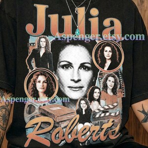 May include: A graphite-coloured t-shirt featuring a large graphic print of Julia Roberts. The design includes multiple black and white photographic portraits of the actor, a film reel, a stack of books, and a movie clapperboard. The text reads Julia Roberts.
